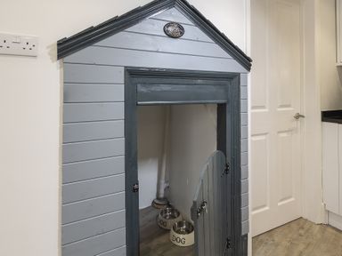 A dog house with two dog bowls inside next to a white door at The Old Wash House in Dartmouth