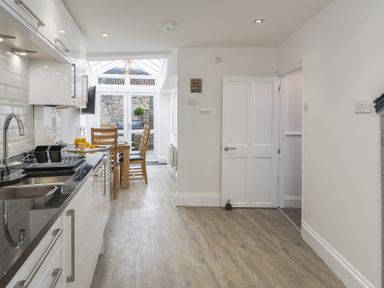 A kitchen with black countertop and white cabinets leading to a dining area with wooden table and chairs at The Old Wash House in Dartmouth