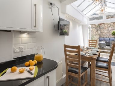 A kitchen with wooden table and chairs and a cutting board with oranges and a jug of juice at The Old Wash House in Dartmouth