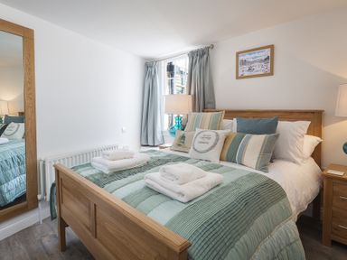 A bedroom with a wooden bed with striped bedding and pillows a large mirror on the wall and bedside tables with lamps at The Old Wash House in Dartmouth