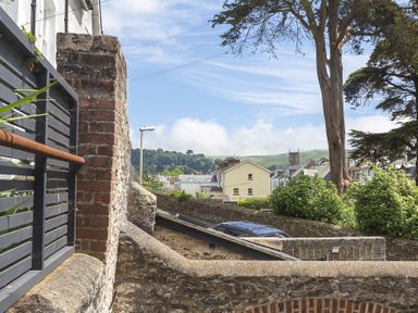 A stone wall with a metal gate and parked car with houses and trees in the background at The Old Wash House in Dartmouth