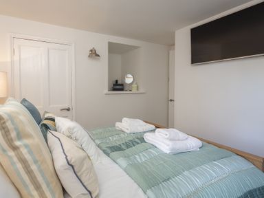 A bedroom with a bed made with folded white towels and pillows and a wall-mounted TV at The Old Wash House in Dartmouth