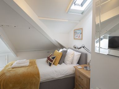 A bedroom with a bed with pillows and a yellow blanket next to a wooden nightstand and a wall mirror at The Old Wash House in Dartmouth