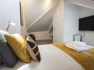 A bedroom with pillows and folded towels on a bed and a wall mounted TV at The Old Wash House in Dartmouth