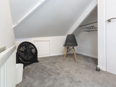 A small room with a fan a black chair a clothes rail with hangers and a waste bin at The Old Wash House in Dartmouth