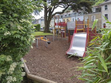 A playground with a slide and climbing structure surrounded by houses at The Old Wash House in Dartmouth