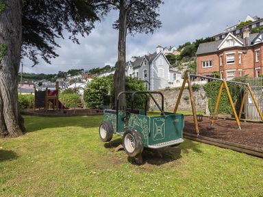 A playground with a toy car and swings surrounded by houses at The Old Wash House in Dartmouth