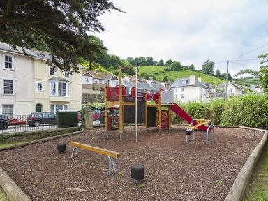 A small outdoor playground with a slide and climbing equipment in a residential area at The Old Wash House in Dartmouth
