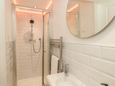 A bathroom with a shower enclosure a round mirror a towel rack and a sink at The Old Wash House in Dartmouth