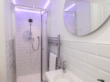A bathroom with a shower enclosure a round mirror a washbasin and a towel rack at The Old Wash House in Dartmouth