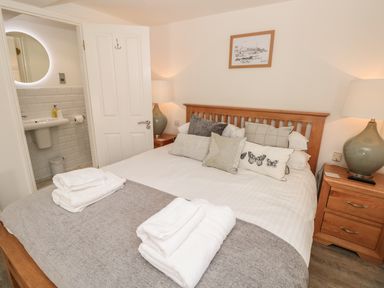 A bedroom with a double bed pillows towels bedside tables lamps and an open door showing a bathroom at The Old Wash House in Dartmouth