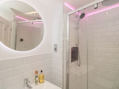 A bathroom with a round mirror above a sink and a glass shower enclosure with a showerhead at The Old Wash House in Dartmouth