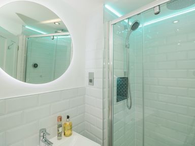 A bathroom with a round mirror a sink with soap and a bottle and a glass shower with a showerhead at The Old Wash House in Dartmouth