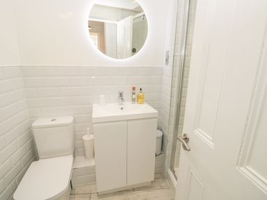 A bathroom with a toilet a sink cabinet a round illuminated mirror and a shower at The Old Wash House in Dartmouth