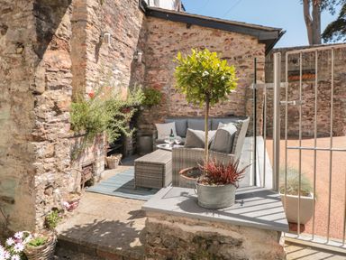 An outdoor seating area with a sofa and table surrounded by stone walls and plants at The Old Wash House in Dartmouth