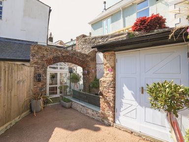 An outdoor area with a stone arch wooden gate potted plants and white double doors at The Old Wash House in Dartmouth