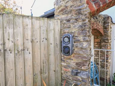 A stone wall with an electric vehicle charger mounted next to a wooden fence at The Old Wash House in Dartmouth