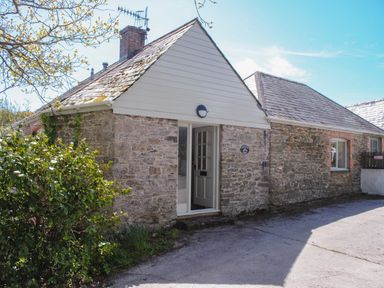 A stone cottage with a white door and a bush beside it at Orchard Barn in Salcombe