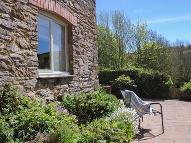 Stone wall with window beside garden and patio with chair and blanket at Orchard Barn in Salcombe