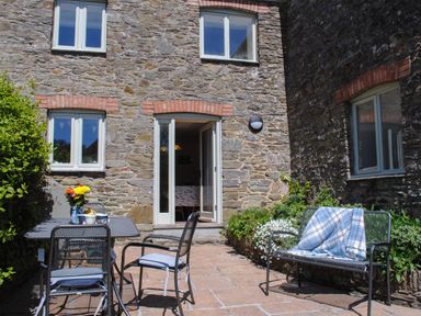 A stone patio with metal chairs and a table with flowers outside a house at Orchard Barn in Salcombe