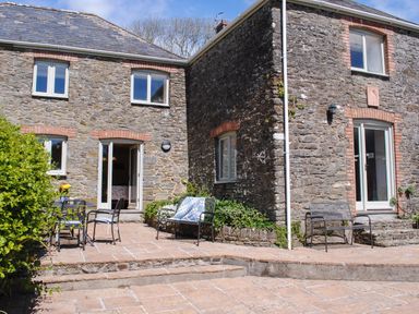 A stone house with outdoor chairs tables and plants at Orchard Barn in Salcombe