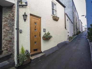 A narrow street with a wooden door numbered 5 and flower pots on the walls at Pixie Cottage in Dartmouth