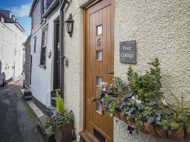 A wooden door with the number 5 and a sign saying Pixie Cottage with flowers in a planter on a street in Dartmouth