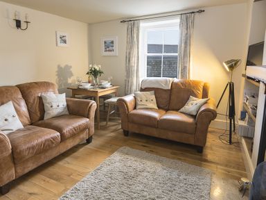 A living room with two brown leather sofas a wooden floor and a dining table at Pixie Cottage in Dartmouth
