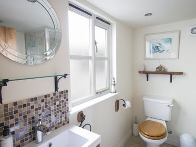 A bathroom with a toilet with a wooden seat a sink with mosaic tiles and a round mirror at Pixie Cottage in Dartmouth