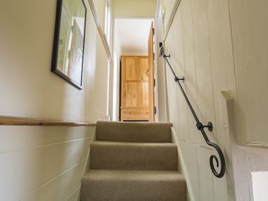 A staircase with beige carpet and black handrail leading to a wooden wardrobe at Pixie Cottage in Dartmouth