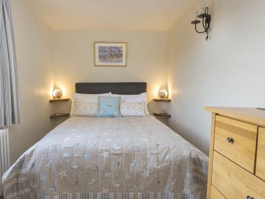 A bedroom with a bed with seashell patterned bedding and wooden dresser at Pixie Cottage in Dartmouth