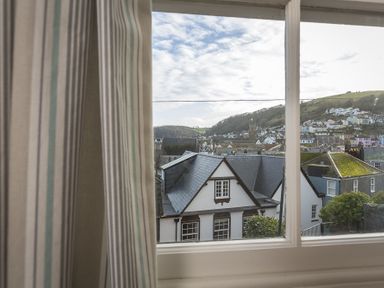 A view of rooftops and houses through a window with striped curtains at Pixie Cottage in Dartmouth