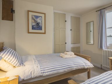 A bedroom with two single beds striped bedding towels on bed a framed picture on wall at Pixie Cottage in Dartmouth