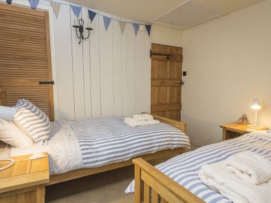 A bedroom with two single wooden beds with striped bedding towels on beds wooden door and bedside tables with lamps at Pixie Cottage in Dartmouth