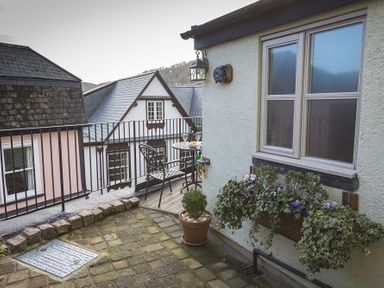 A balcony with a table and chairs next to a building with a window planter at Pixie Cottage in Dartmouth