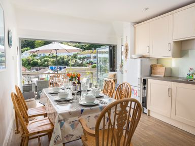 A dining area with a table set for six and a kitchen with light cabinets at Prospects in Salcombe