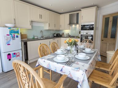 A kitchen with dining table set with plates bowls glasses and flowers at Prospects in Salcombe