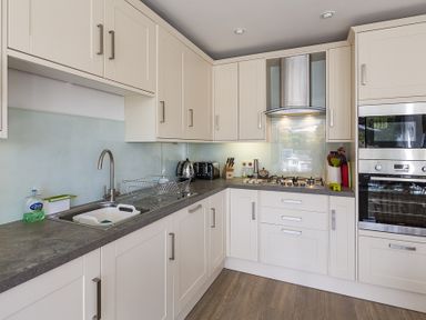 A kitchen with white cabinets a gray countertop a sink a gas stove a built in oven and kitchen utensils at Prospects Salcombe