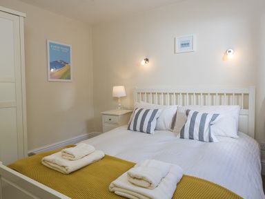 A bedroom with a double bed with white and striped pillows yellow blanket and towels on the bed at Prospects Salcombe