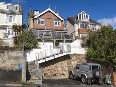Exterior view of three houses with stairs, railings, plants, and a parked silver vehicle on the street at Prospects in Salcombe
