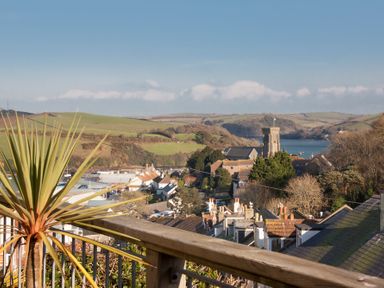 A view of rooftops trees and a church with hills and water in the background at Prospects in Salcombe