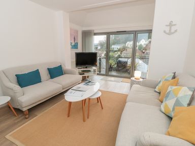 A living room with two sofas a coffee table a television and glass doors leading to a balcony at Prospects in Salcombe
