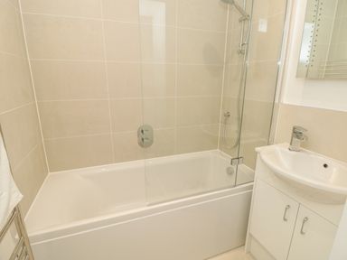 A bathroom with a bathtub shower combination and a sink with cabinet at Prospects in Salcombe