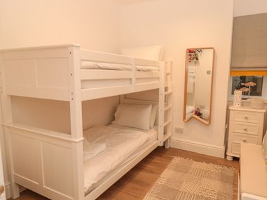 A bedroom with a white bunk bed a mirror on the wall a small white drawer and a patterned rug on the floor at Prospects in Salcombe
