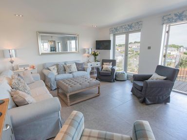 A living room with sofas armchairs a large ottoman and a wall mirror at Raleigh House in Salcombe
