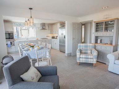 A kitchen and dining area with a table set for breakfast and armchairs at Raleigh House in Salcombe