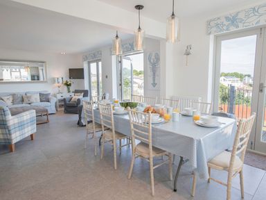 A dining room with a table set for breakfast and a living area with sofas at Raleigh House in Salcombe