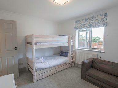 A bedroom with bunk beds a window a gray sofa and a door at Raleigh House in Salcombe