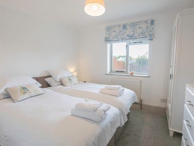 A bedroom with two single beds a window with a patterned blind and white furniture at Raleigh House in Salcombe