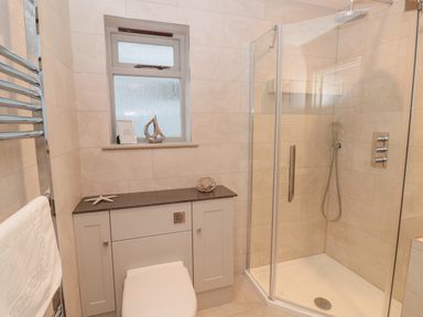 A bathroom with a glass shower enclosure a toilet and a cabinet under a frosted window at Raleigh House in Salcombe